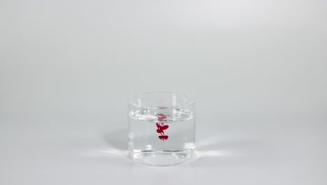 el tinte rojo se extiende lentamente en un vaso de agua transparente