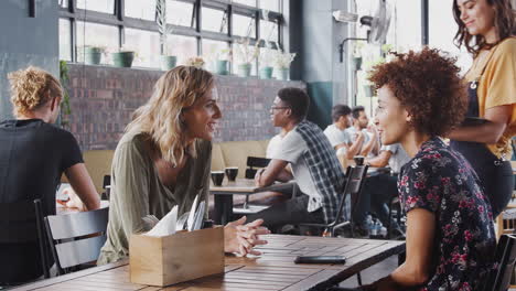 Zwei-Freundinnen-Sitzen-Am-Tisch-Im-Café-Und-Werden-Von-Einer-Kellnerin-Bedient