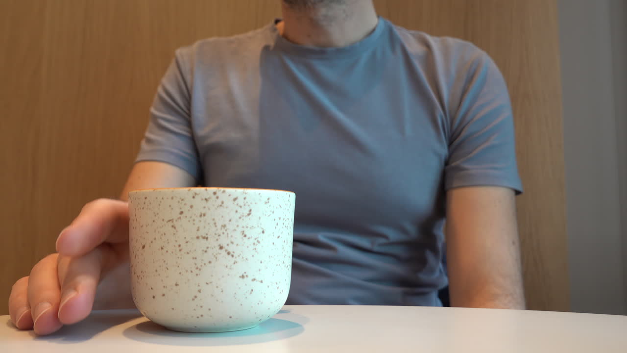 Man in grey shirt drinking a beverage from a white cup at a cafe