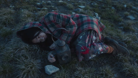 melancholic woman lying on grass near lantern in evening outdoors