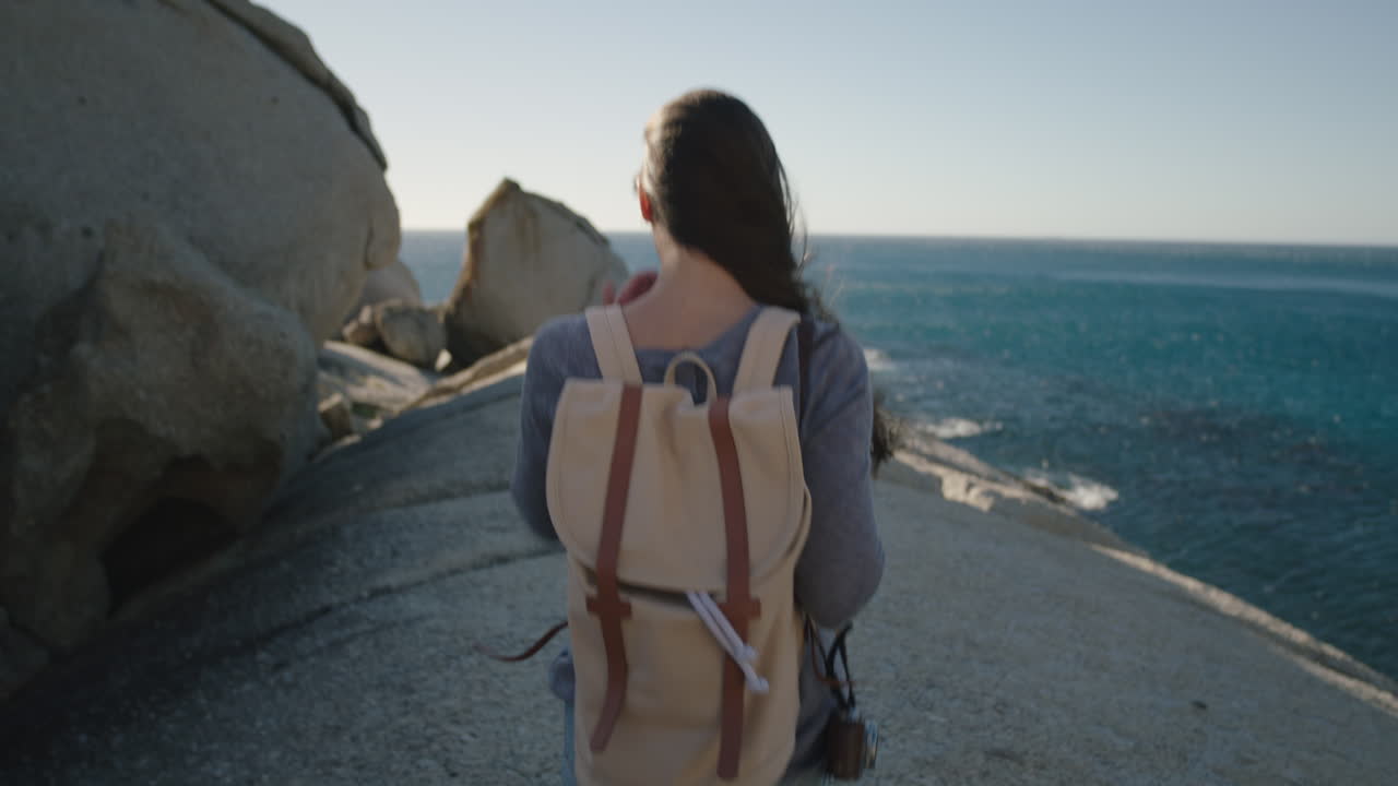 primer plano de una mujer joven y valiente caminando por la hermosa costa del océano disfrutando de la aventura explorando un estilo de vida de vacaciones independientes con mochila