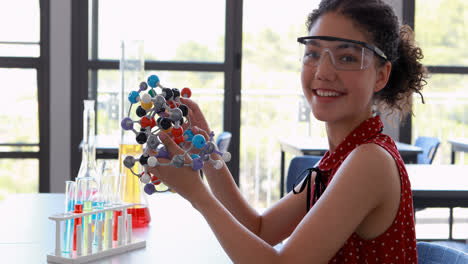 Portrait-of-happy-schoolgirl-experimenting-molecule-model-in-laboratory