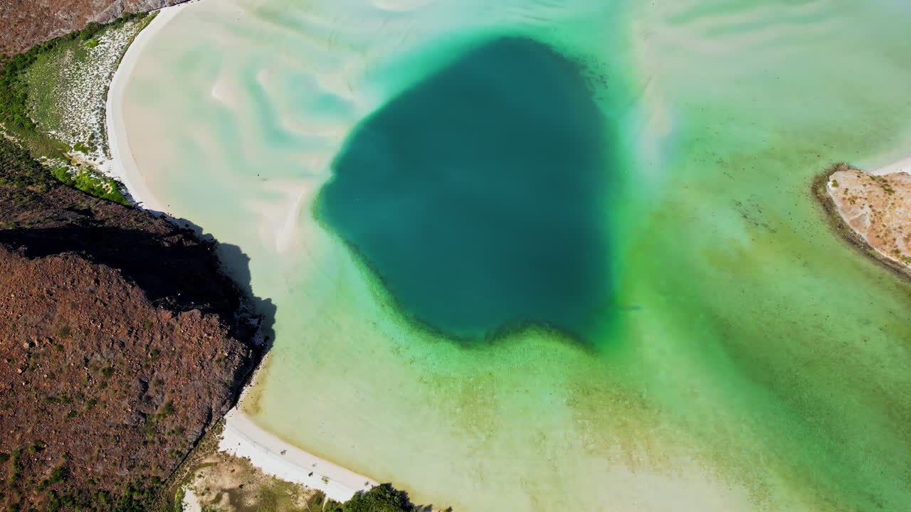 Aerial drone view of crystal clear blue waters with desert mountains in the background along the Baja California coast