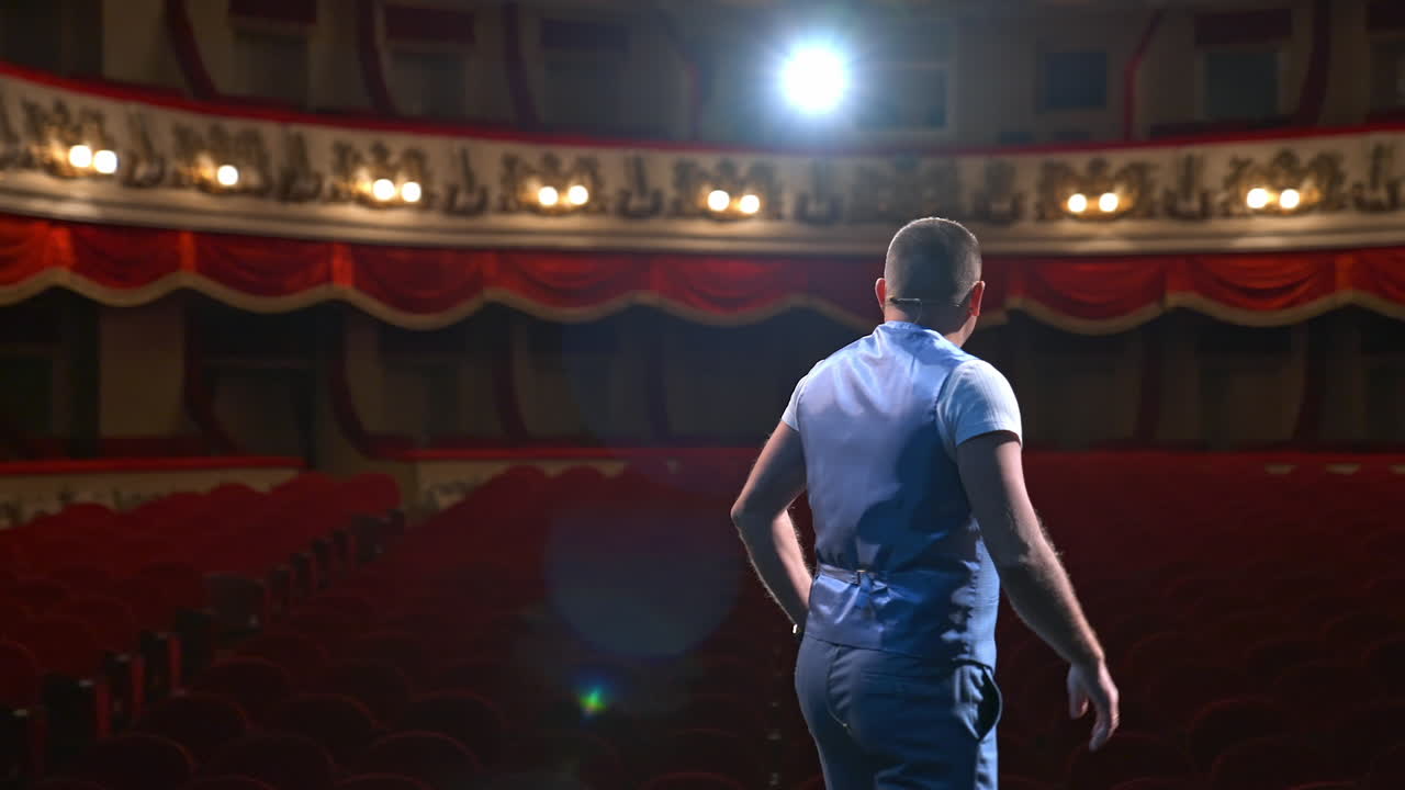 Actor rehearsing his role. Male speaker performing in front of empty auditorium in theater against bright spotlight. Back view.