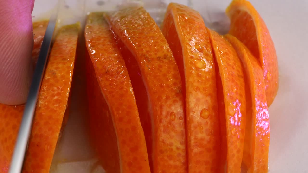 Knife cutting half tangerine in slices. Macro shot close up in white surface.