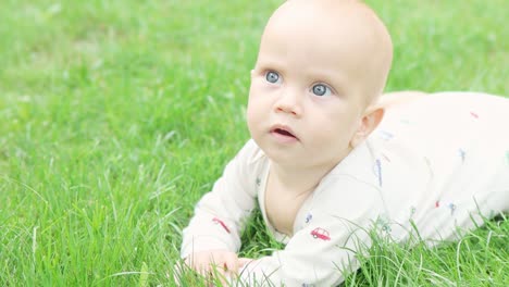 funny baby child lying on green grass garden, making face, smiling, exploring