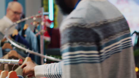 Helpful-worker-wearing-Santa-hat-in-festive-Christmas-decorated-clothing-shop,-offering-shopping-advice-to-confused-elderly-client.-Retail-assistant-talking-with-woman-in-fashion-boutique