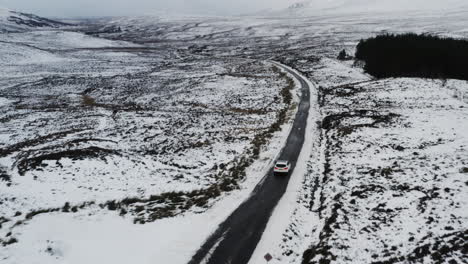 Die-Hochwinklige-Luftbildverfolgung-Verfolgt-Die-Fahrt-Eines-Weißen-Geländewagens-Durch-Eine-Zerklüftete-Landschaft-Aus-Schnee-Und-Eis