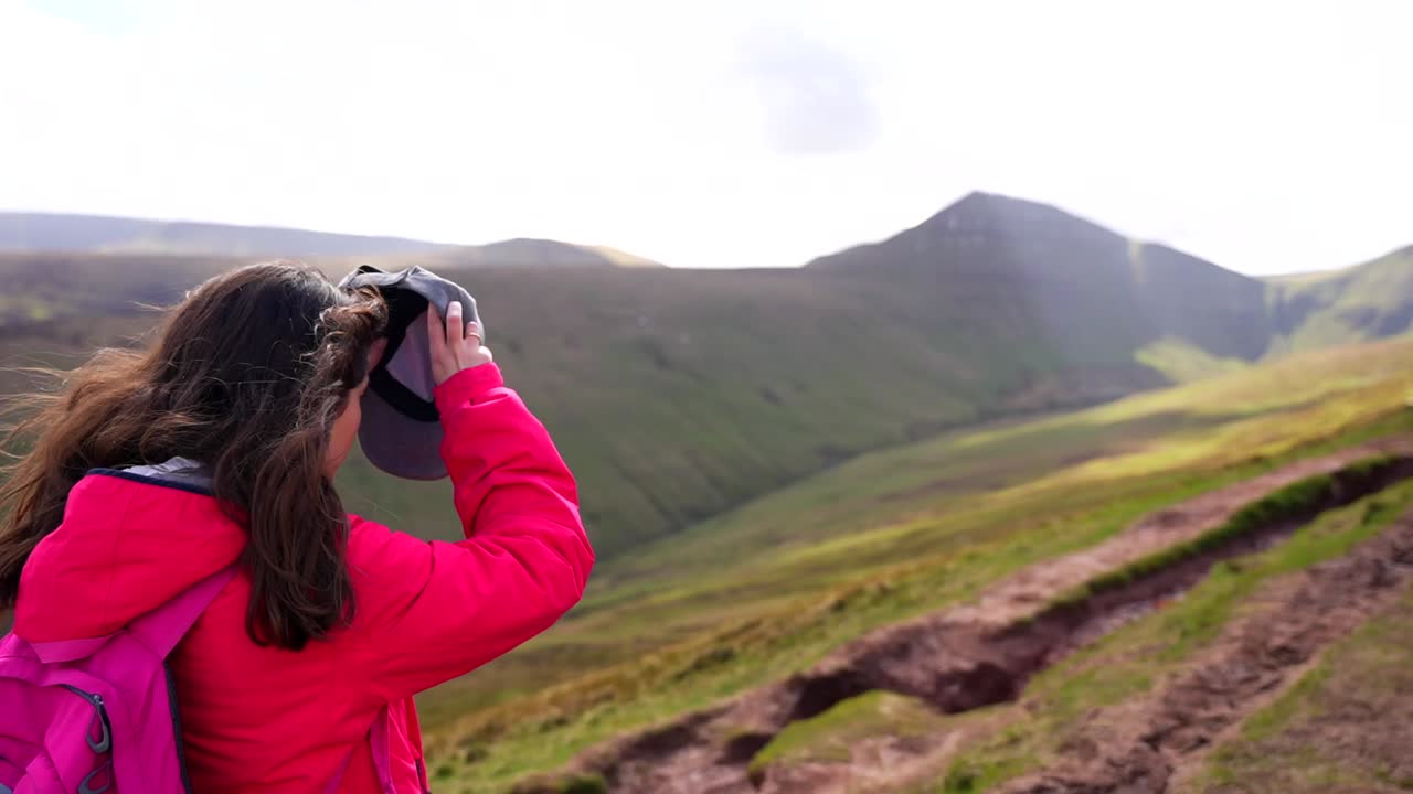 una mujer mochilera se pone una gorra y camina hacia la montaña pen y fan en un día soleado