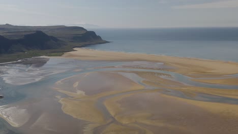 aerial view of sandy raudasandur beach with rocky coastline during sunny day - backwards shot