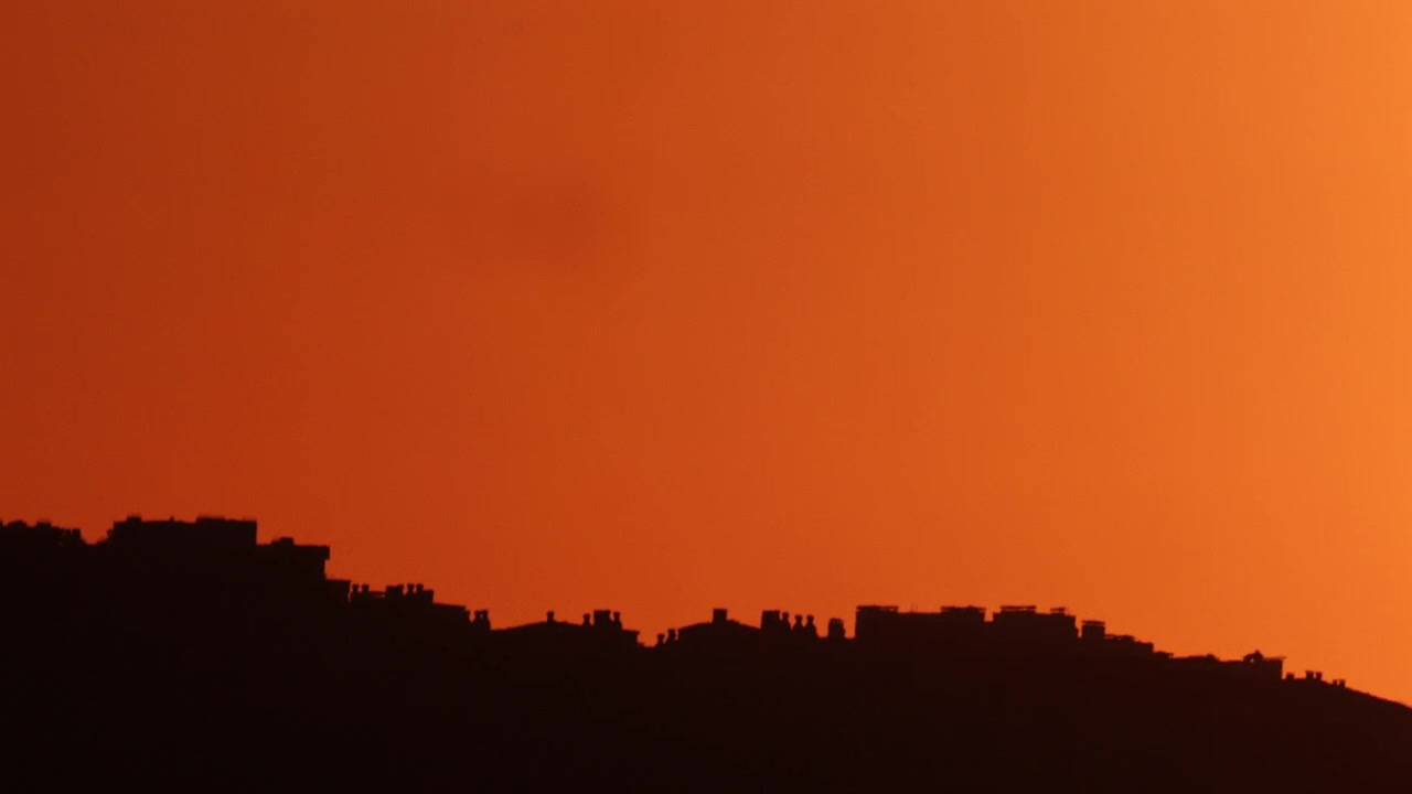 Silueta de un horizonte urbano contra un cielo de atardecer naranja intenso