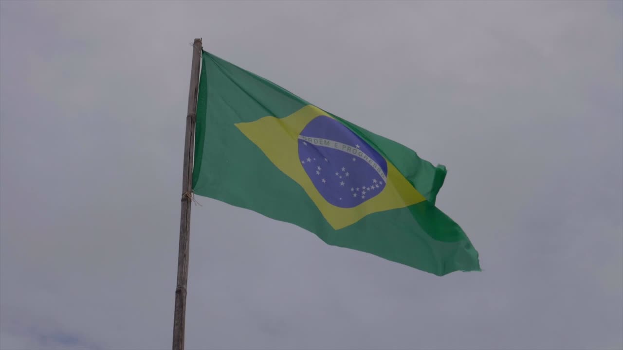 Slowmotion af brasiliansk flag, der blafrer i vinden mod overskyet himmel