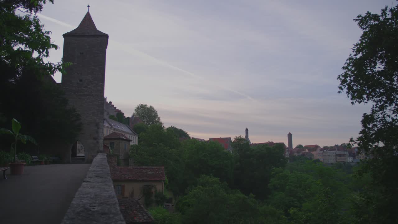 Stone tower rising above the rooftops of Rothenburg ob der Tauber, Germany, at dawn, surrounded by lush trees