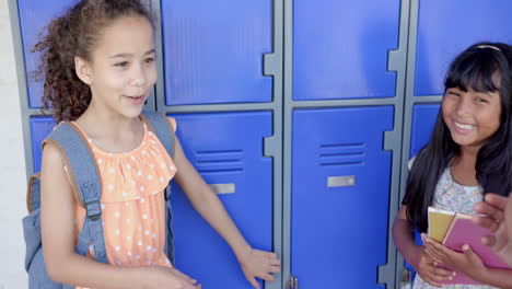 in school, two girls smiling and talking near blue lockers, holding books