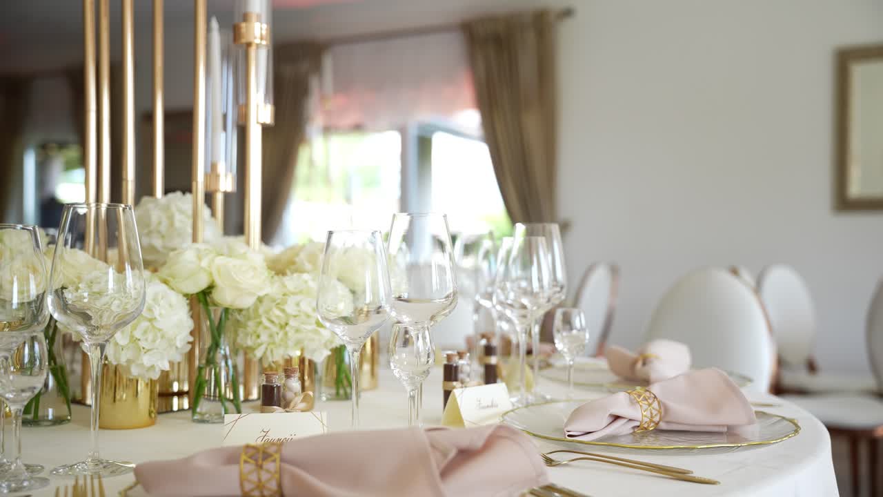 Elegant wedding reception table setup with white floral centerpieces, gold accents, and blush napkins, creating a luxurious and romantic ambiance