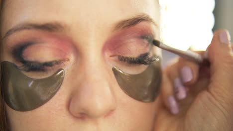 make-up artist put on shadows on a eyelid. light hair model. close up view. smoky eyes, gold patches under eyes