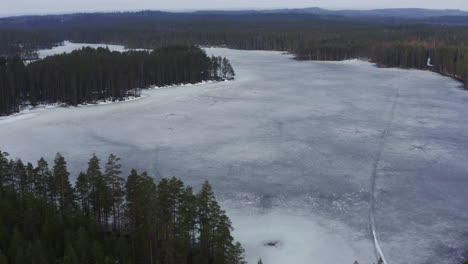 Aerial-drone-view-of-dangerous-black-thin-ice-in-a-lake-by-springtime,-with-snowmobile-tracks-and-natural-holes-in-the-ice-that-looks-like-small-meteor-hits