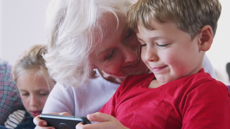 grandmother playing video game with grandson on mobile phone at home