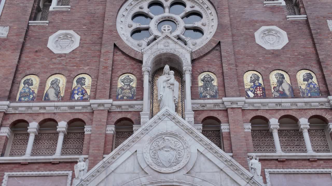 Close-up view of the Votive Church facade in Szeged, Hungary, showcasing detailed sculptures of religious people and ornate architectural design