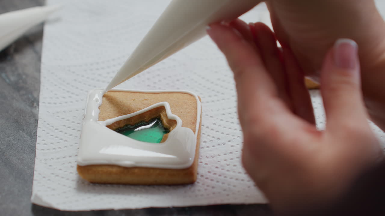 초록색으로 채워진 쿠키에 섬세한 아이싱 프로세스의 클로즈업, 텍스처 된 종이에 배치, 미세한 파이핑 기술과 장식, 하 아이싱이 설계 주변에 조심스럽게 파이핑됩니다.