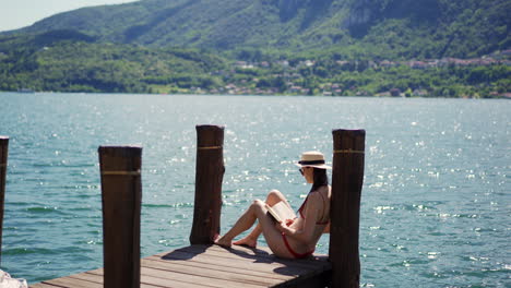 a beautiful woman reads a book by lake orta in italy. warm summer sun and vacation. surrounded by the natural beauty of the italian countryside and hills.