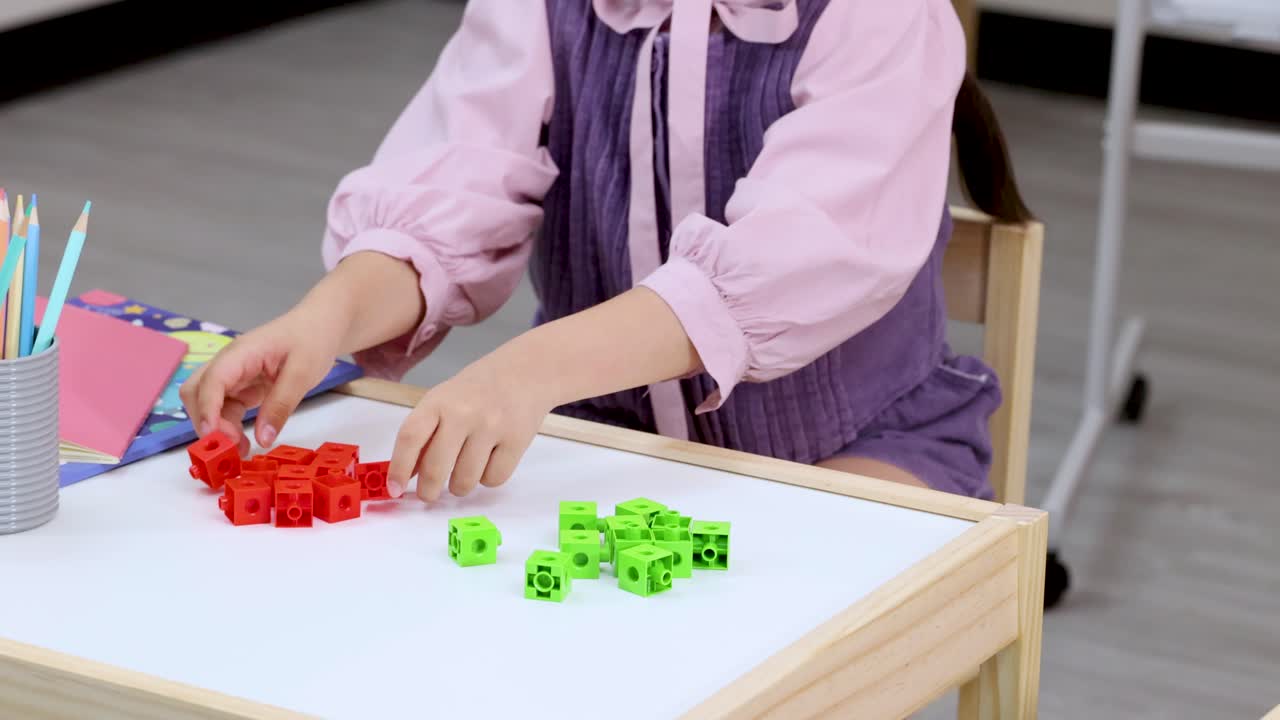 Young student organizes red and green counting cubes on classroom table with static overhead framing