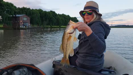 a girl holding a bass she caught on a calm lake during sunset