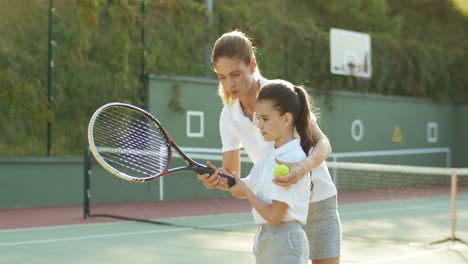 Liebevolle-Frau,-Die-Ihrer-Süßen-Kleinen-Tochter-Beibringt,-Wie-Man-An-Einem-Sommertag-Auf-Dem-Sportplatz-Tennis-Spielt-1