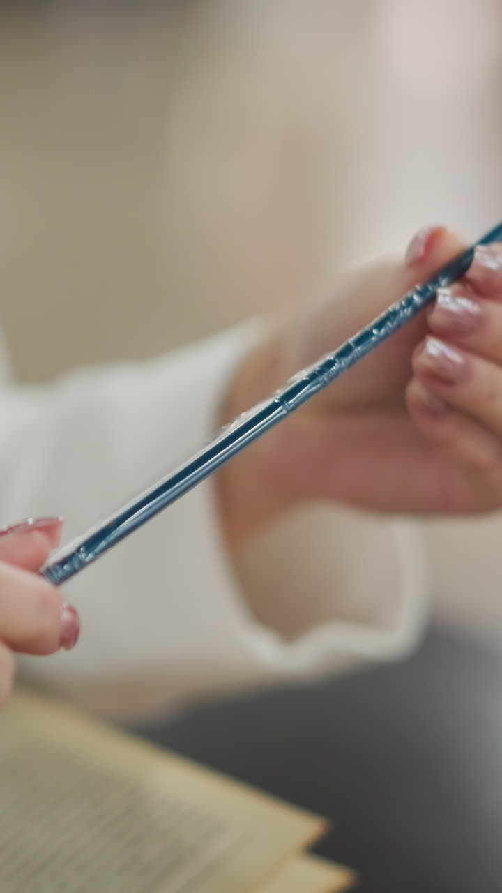 primer plano de manos sosteniendo una paja azul mientras la observan cuidadosamente, el fondo presenta una escena de compras borrosa con bolsas de compras de menta y verdes