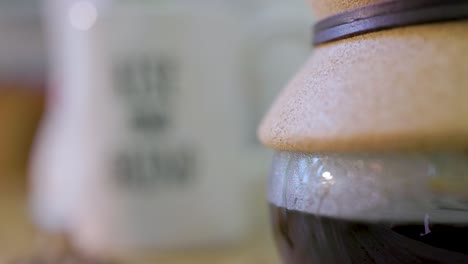 vista de cerca un vaso de café chemix que el estante se centra en una taza de café blanca que lee subir y moler para significar la entrada y salida de una taza de café