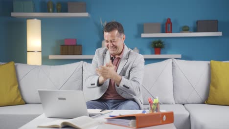un trabajador de oficina en casa aplaudiendo lo que ve en la computadora portátil.
