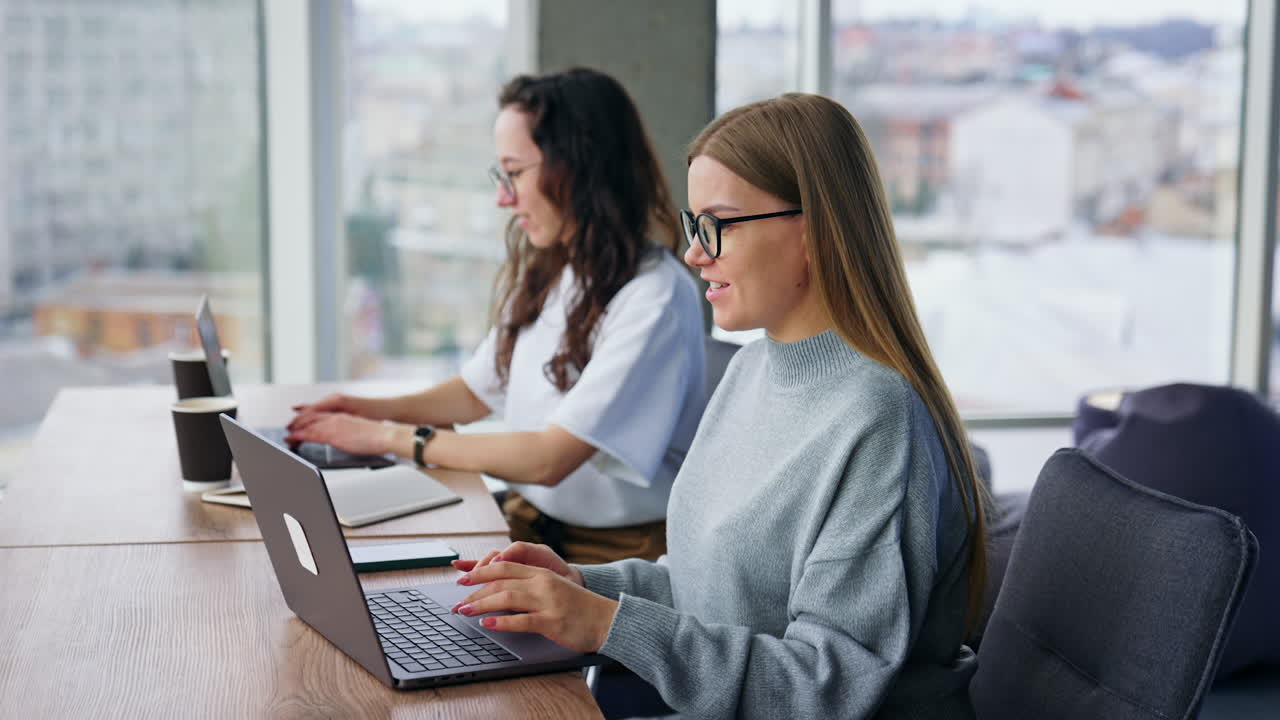 Positive young female colleagues work at laptops in the office. Calm working atmosphere.