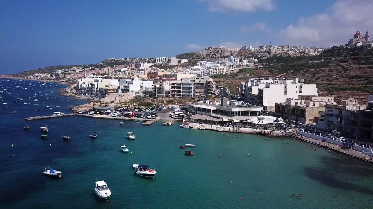 Veduta aerea del villaggio di Mellieha, della Baia di Ghadira e di molte barche a Malta. Mare Mediterraneo e spiaggia. La telecamera del drone si sposta all'indietro