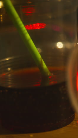 Vertical-Video-Close-Up-Of-Plastic-Cup-With-Alcohol-And-Drinking-Straw-On-Table-At-House-Party