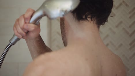 white man with dark hair washes himself with the shower head in his hair