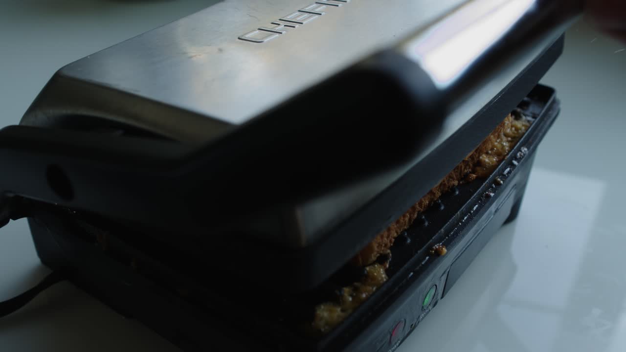 A pice of white bread with butter spread over it is place on top of the marble cheese for the grilled cheese, then the panini press is closed to grill the sandwich