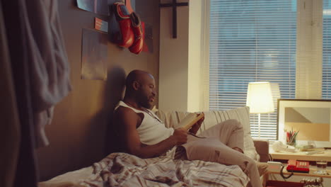 african american man reading book on bed at home