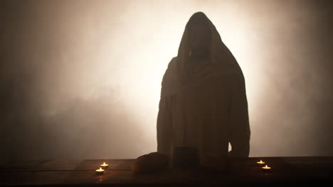 the silhouette of jesus christ standing near a table with christian sacraments of bread and wine for last supper, communion, easter symbolism. in cinematic slow motion with ambient light.