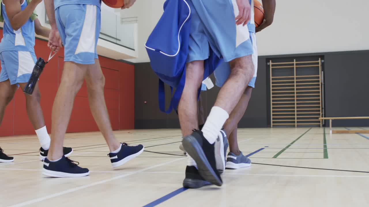 Squadra di basket maschile eterogenea che si allena con un allenatore maschio in un campo al coperto, al rallentatore