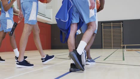 diverse male basketball team training with male coach in indoor court, in slow motion