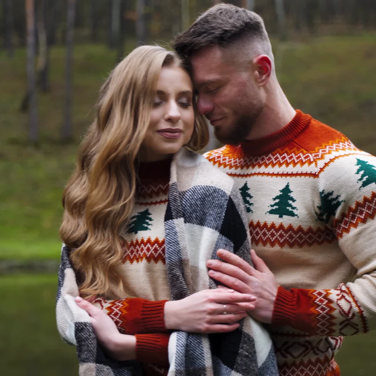 Giovane uomo ha abbracciato e coperto la ragazza con una coperta. Bella coppia all'aperto. Sfondo di natura autunnale.