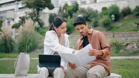 Ernstes-Paar-Arbeitet-Vertikal-An-Arbeitspapieren-Im-Park.-Partner-Arbeiten-Auf-Einer-Bank-Zusammen