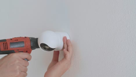 las manos del hombre usan un taladro eléctrico e instalan una cámara de cctv en la pared para la seguridad.
