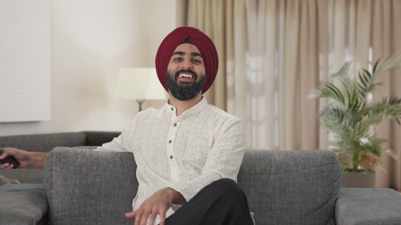 Felice uomo indiano Sikh che ride mentre guarda la TV