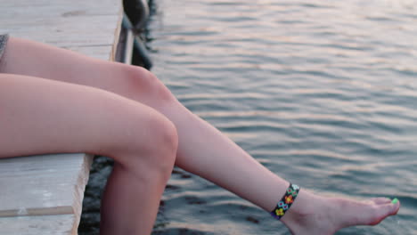 woman sitting on lake pier and swinging legs in water