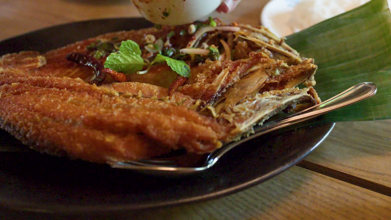 Spicy chili herb sauce poured onto crispy fried fish on banana leaf plate, natural lighting