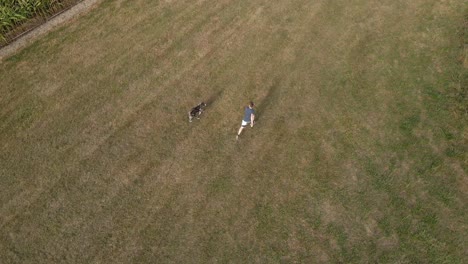 Man-being-chased-by-his-shepherd-dog-in-rural-green-field