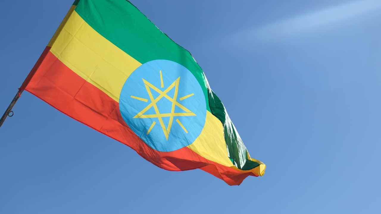 Ethiopian flag, featuring green, yellow, and red stripes with the national emblem, waving against a clear blue sky in Addis Abeba, symbolizing national pride and sovereignty, slow motion shot