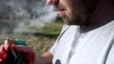 close up caucasian man with bloody hand holding and smoking a cigarette, slow motion