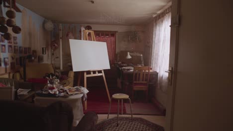 slow push in into a chaotic artist studio, with an empty canvas in the middle of the room